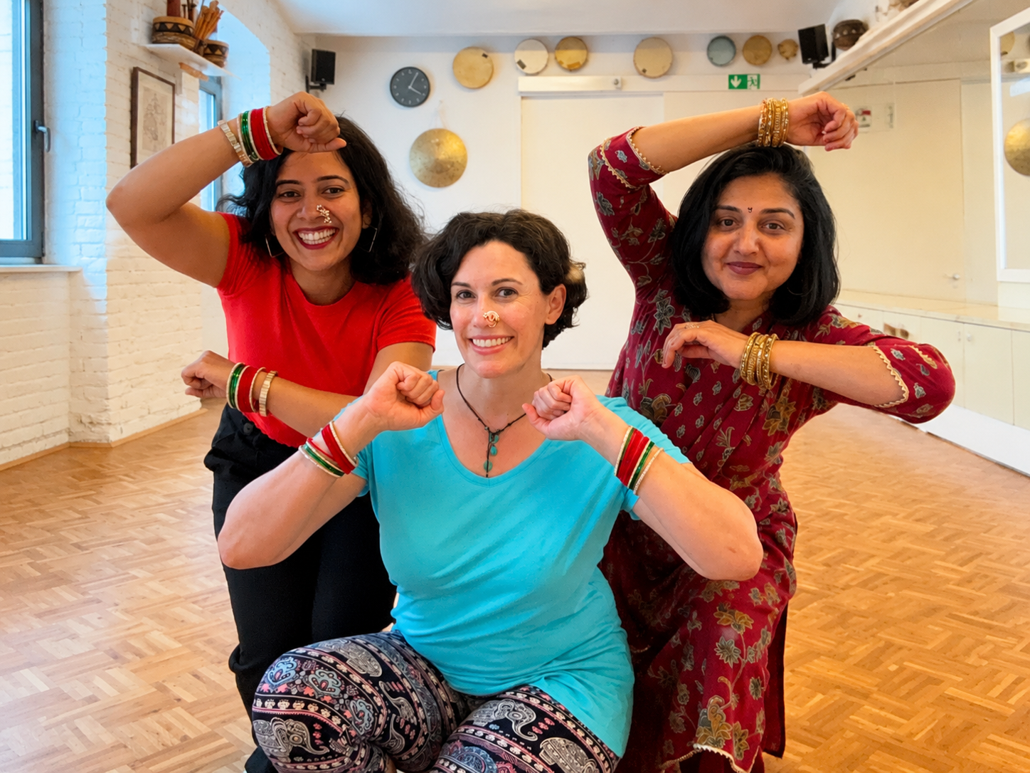 Three participants practicing Bollywood dance poses together in a studio
